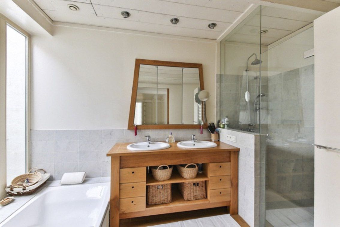 Baño con lavabo doble de madera y un espejo de corte irregular